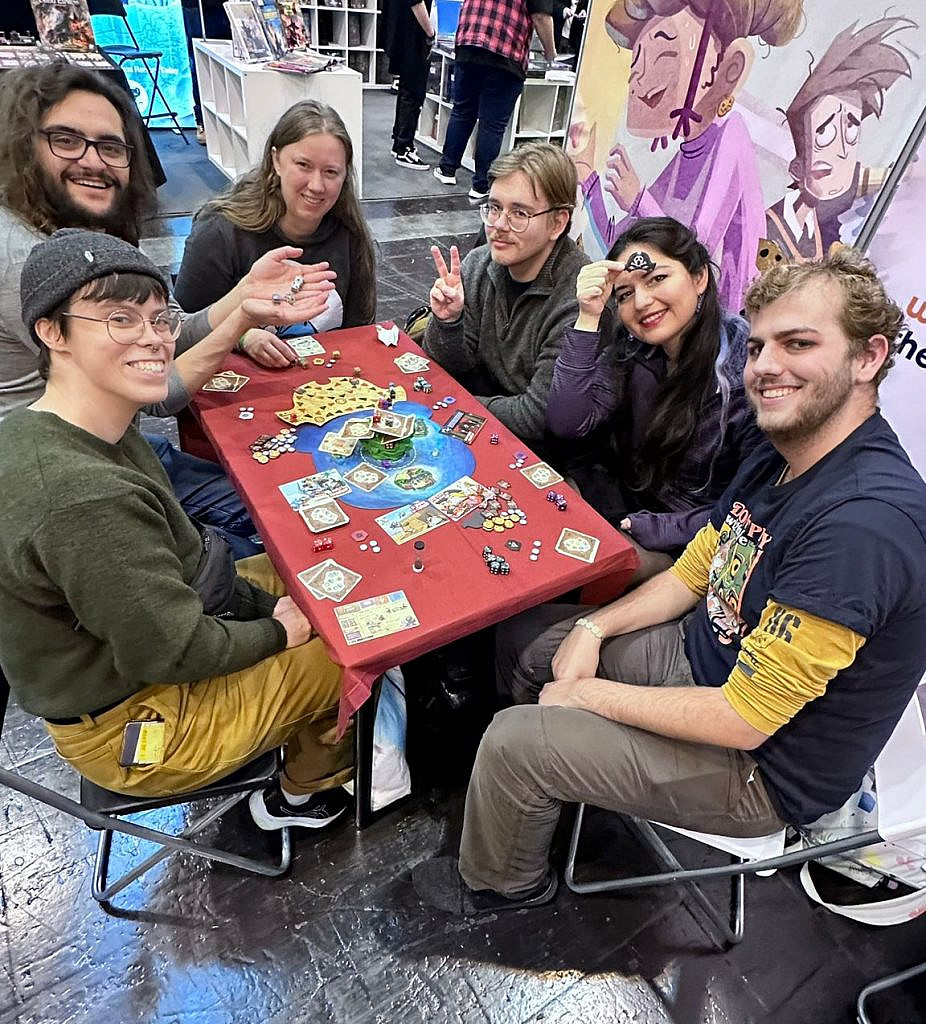 A game table with six people around it, half of them are female presenting