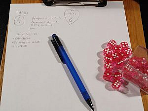 A simple character for a tabletop roleplaying game, written on a piece of paper on a notepad. There is also a blue pen and a stack of red dice laying on the paper.