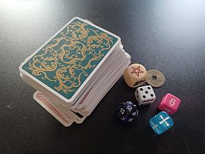 A deck of cards, various dice and a coin, laid out on a table. 